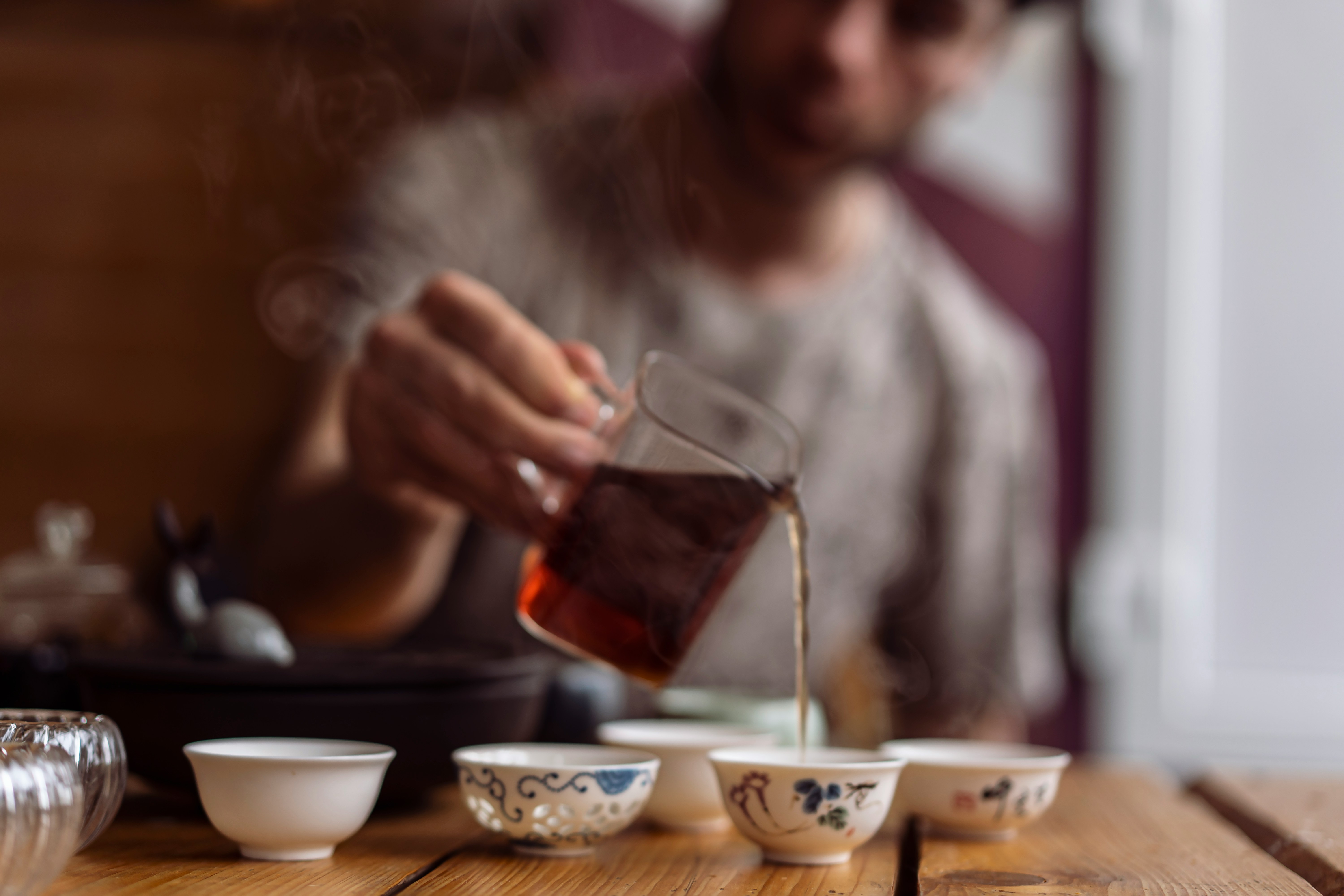 Fresh black tea being poured from a glass teapot into small tea cups